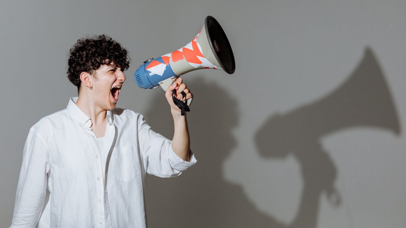 curly haired man shouting through megaphone