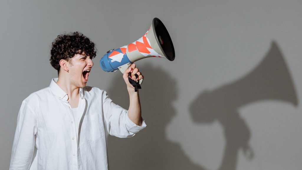 curly haired man shouting through megaphone